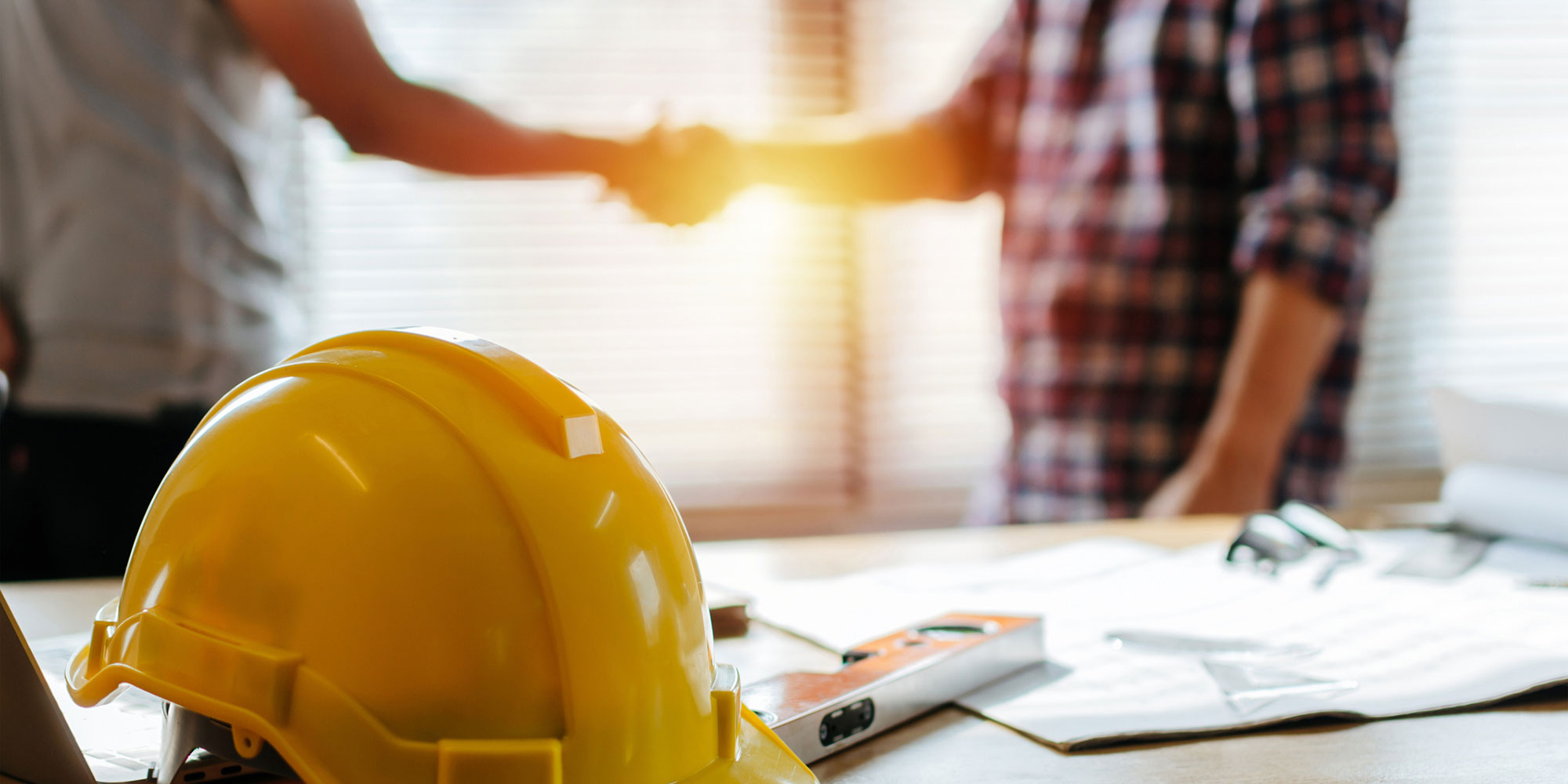 Two men shaking hands with hardhat in the foreground